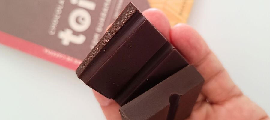 chocolate-bean-to-bar-detalhe-omicha.jpg Imagem aproximada de mão segurando pedaços de chocolate bean-to-bar da marca omicha
