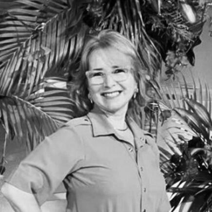 Retrato da nutricionista Nazaré França, uma mulher madura de cabelos claros curtos, usando óculos, sorrindo suavemente para a câmera em depoimento para a OMICHA.